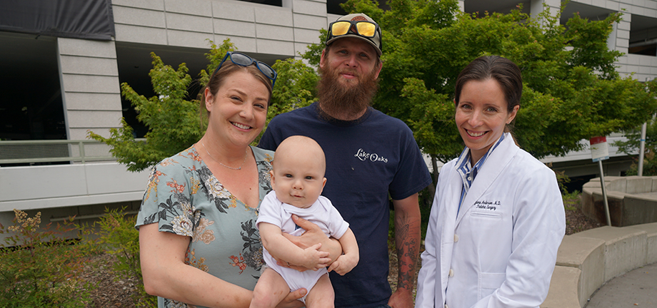 Mom, dad, baby and doctor pose together outside the UC Davis Medical Center parking garage.