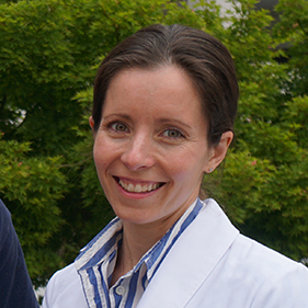 Smiling woman in a white doctor's coat with a blue and white striped shirt