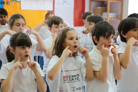 Primary school children make the Italian hand gesture for tasty food