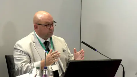 Lampard Inquiry / YouTube Andres Freire-Patino - a man wearing glasses sitting a a desk giving evidence during the inquiry.