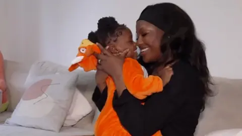 Handout A young baby wearing an orange onesie is held up to her mother's face as the two exchange smiles
