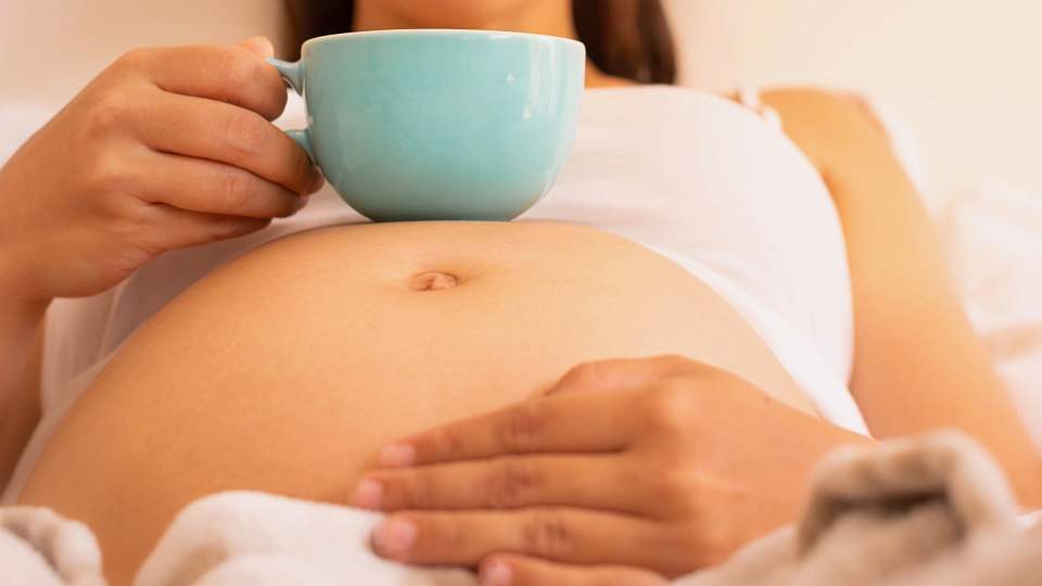 Pregnant person drinking from a mug